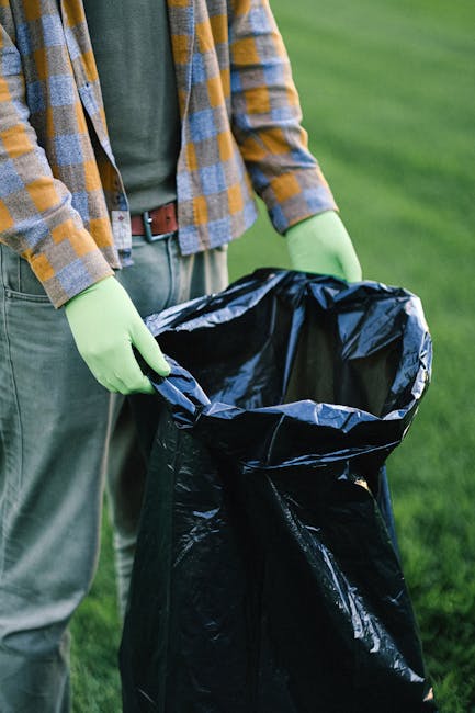 Close-up of tightly knotted black plastic rubbish bags made from shiny, durable polyethylene, stacked against a plain, light-colored wall. The bags are filled with household waste, showing a slightly 